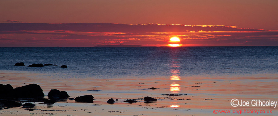 Sunrise at Yellowcraigs Beach. Sun breaking horizon and reflections starting.