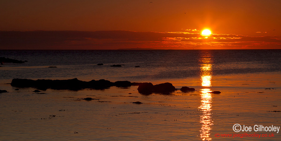 Sunrise at Yellowcraigs Beach. Sun breaking horizon and reflections starting.